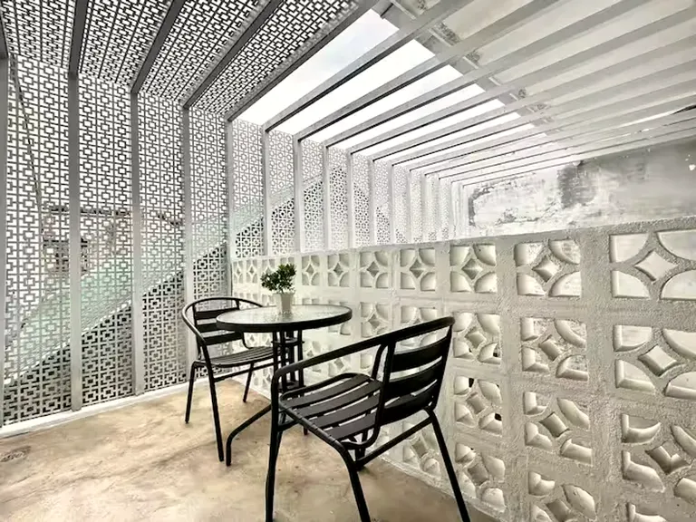 The upstairs terrace wrapped in geometric perforated-aluminium screens, sunlight striping the floor through the slatted pergola.